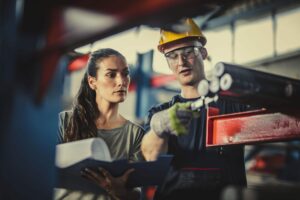 Man and woman brainstorm on the plant floor of the manufacturing plant.