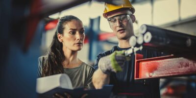 Man and woman brainstorm on the plant floor of the manufacturing plant.