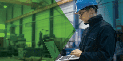 Man working on a laptop ina production environment where the company is working to bridge the IT/OT divide.