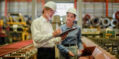 Woman and man in a factory setting up predictive maintenance processes on a tablet and a laptop.