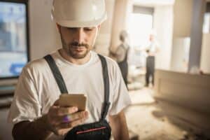 Male worker text messaging on smart phone while being in renovating home.